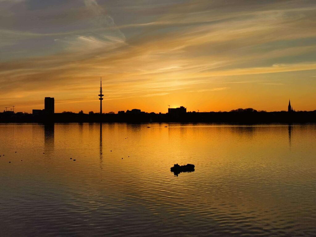 Stadtsilhouette mit Fernsehturm im goldenen Sonnenuntergangslicht, gespiegelt im See