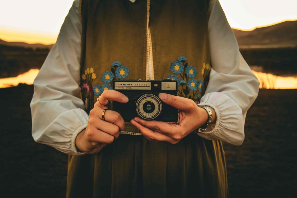 Person hält analoge Kamera in den Händen beim Fotografieren in der goldenen Stunde