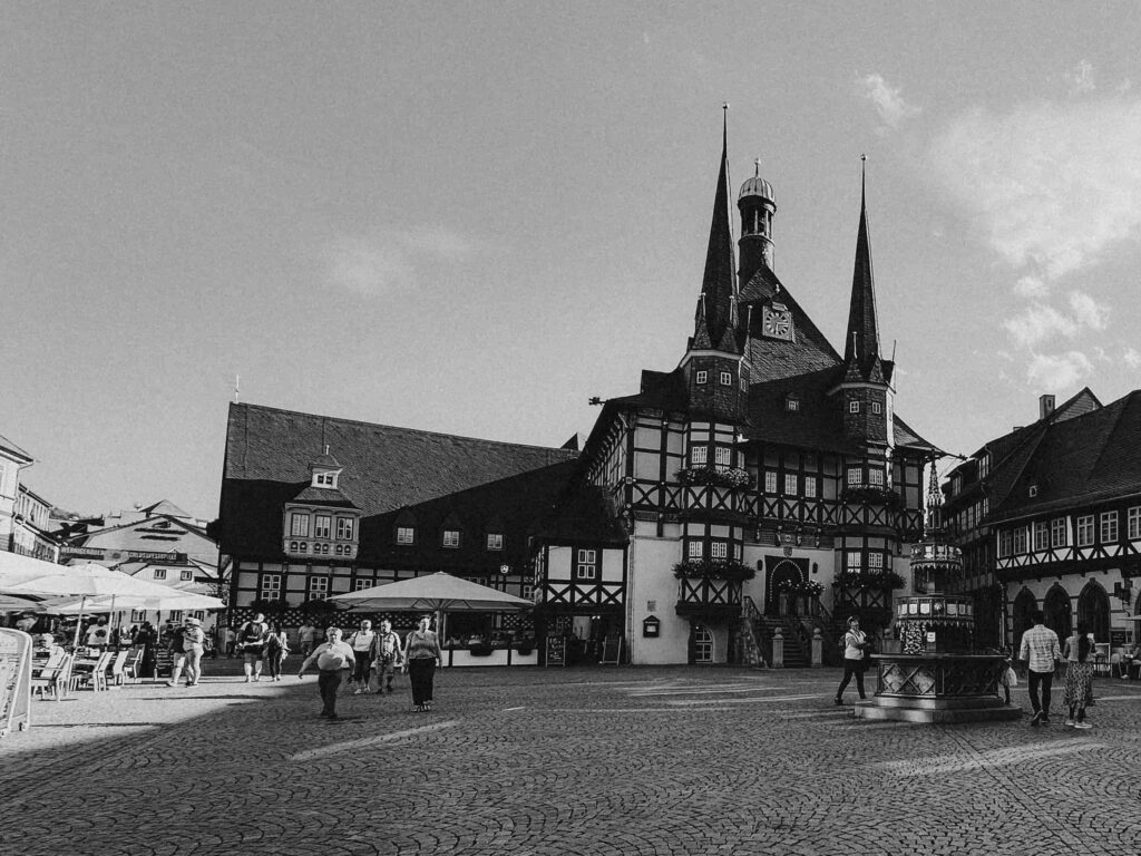 Schwarzweiß-Architekturfotografie: Historisches Fachwerkrathaus auf einem belebten Marktplatz mit Passanten – Beispiel für Kontext und Menschen in der Architekturfotografie