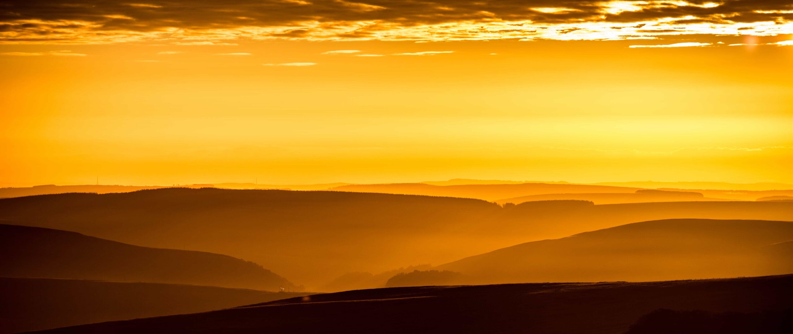 Goldene Stunde: warmes orangefarbenes Licht über einer Hügellandschaft kurz vor Sonnenuntergang