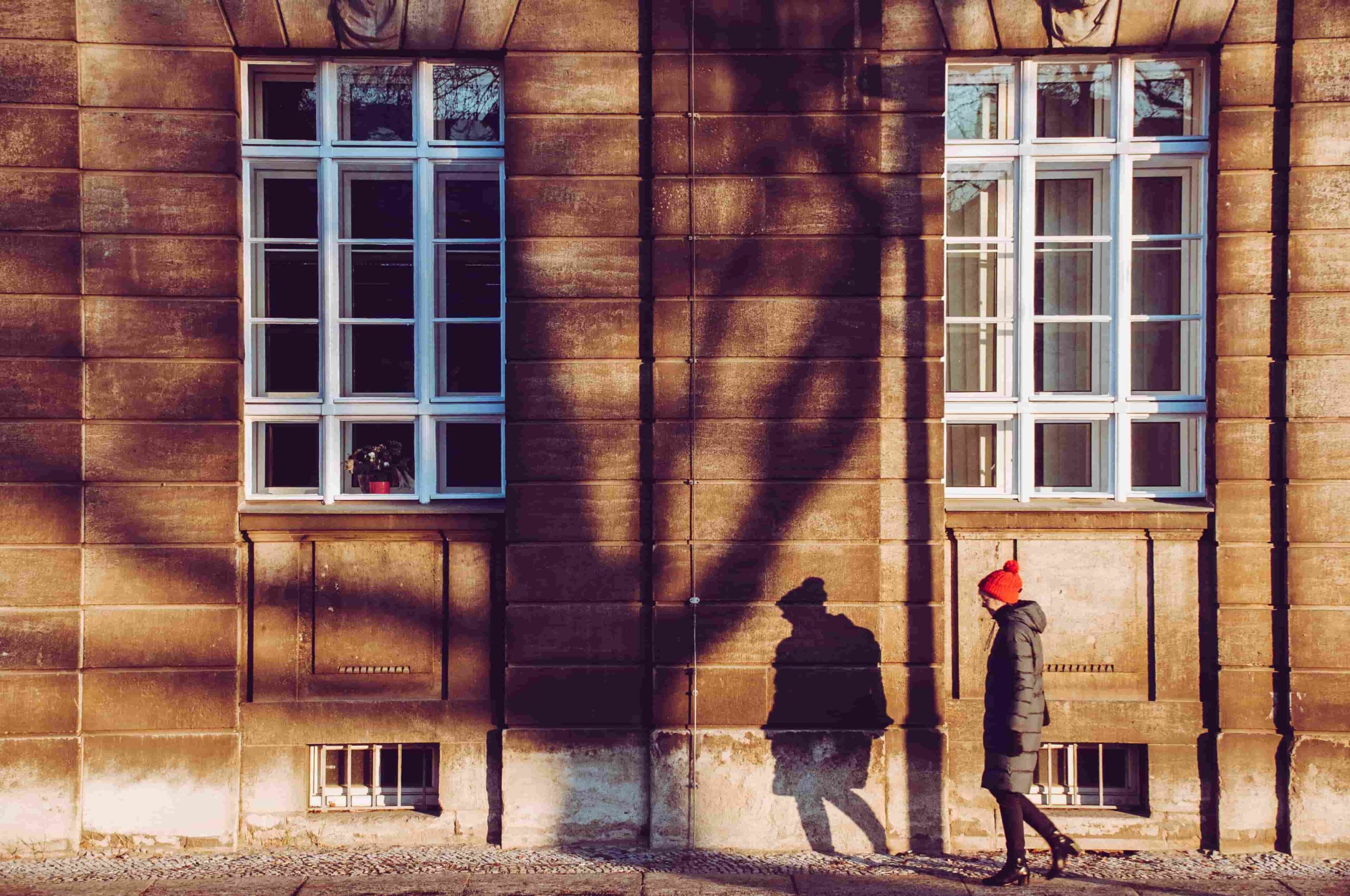 Frau mit roter Mütze vor einer Hausfassade – Beispiel für Bildkomposition mit Schatten, Kontrast und negativem Raum